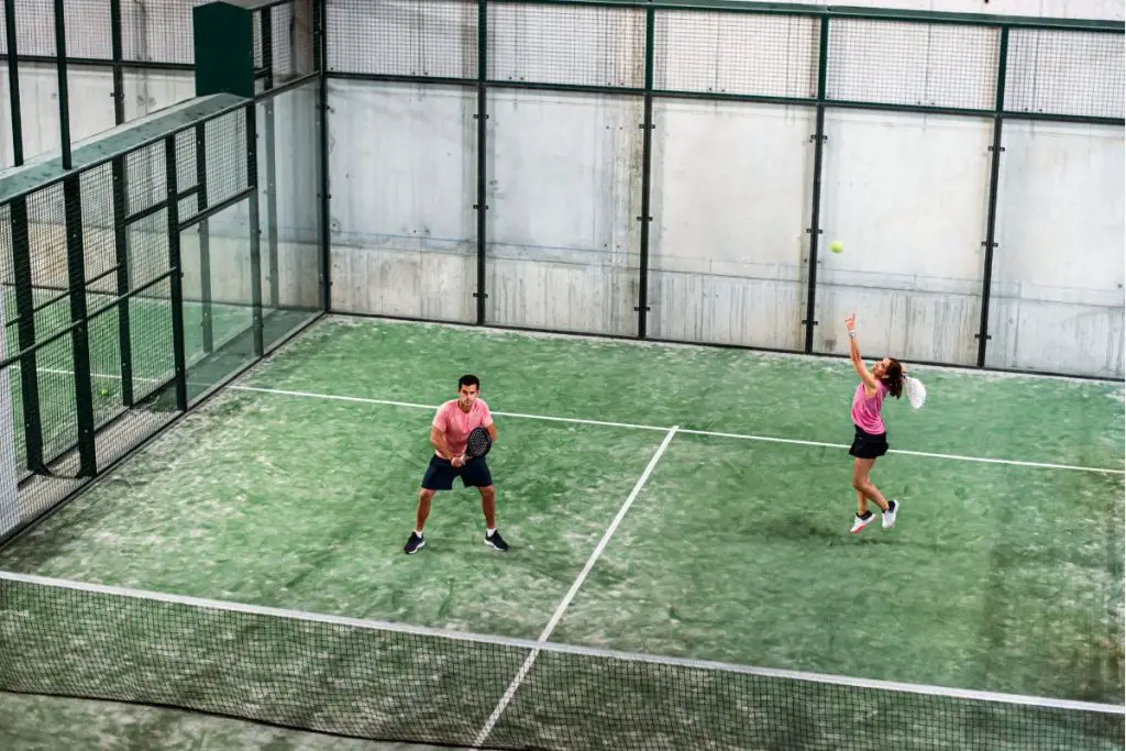 a man and a woman playing padel ball on a court with a green surface
